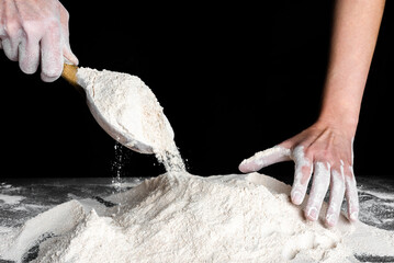 Baker pouring flour with a wooden spoon on kitchen table. Preparing dough for bread or pizza. Baking concept.