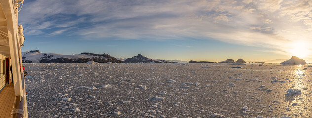Kreuzfahrtschiff fährt bei einen dramatischer Sonneuntergang / Abendstimmung durch die winterliche Cierva Cove - ein tiefer Meeresarm an der Westseite der Antarktischen Halbinsel, umringt von der Cier - obrazy, fototapety, plakaty