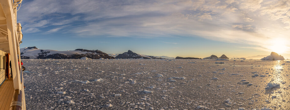 Kreuzfahrtschiff fährt bei einen dramatischer Sonneuntergang / Abendstimmung durch die winterliche Cierva Cove - ein tiefer Meeresarm an der Westseite der Antarktischen Halbinsel, umringt von der Cier