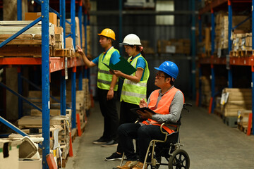 Senior male manager in wheelchair and young workers wearing safety uniform checking quantity of storage product on shelf