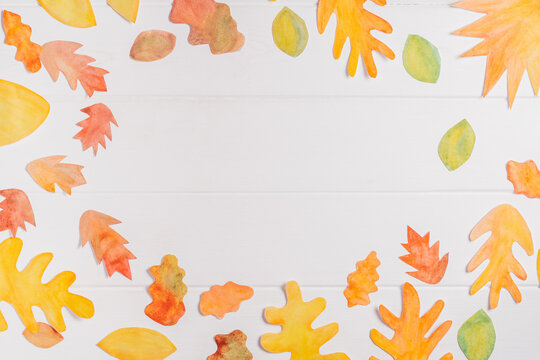 Background image of cut paper red, orange and yellow autumn leaves painted in watercolor laid out on white wooden planks. top view. Copy space. DIY handmade autumn decorations