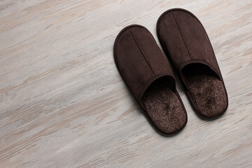 Pair of brown slippers on white wooden floor, top view. Space for text