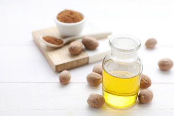 Bottle of nutmeg oil and nuts on white wooden table, closeup. Space for text