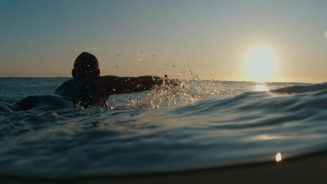 Male surfer paddles in the ocean at sunrise