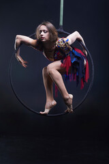 Beautiful woman performing acrobatic element on aerial ring indoors. Circus performer doing trick on arial lira on black background.
