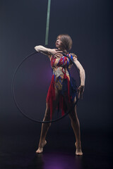 Beautiful woman performing acrobatic element on aerial ring indoors. Circus performer doing trick on arial lira on black background.
