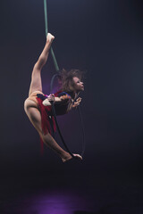 Beautiful woman performing acrobatic element on aerial ring indoors. Circus performer doing trick...