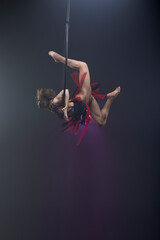 Beautiful woman performing acrobatic element on aerial ring indoors. Circus performer doing trick on arial lira on black background.