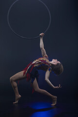 Beautiful woman performing acrobatic element on aerial ring indoors. Circus performer doing trick...