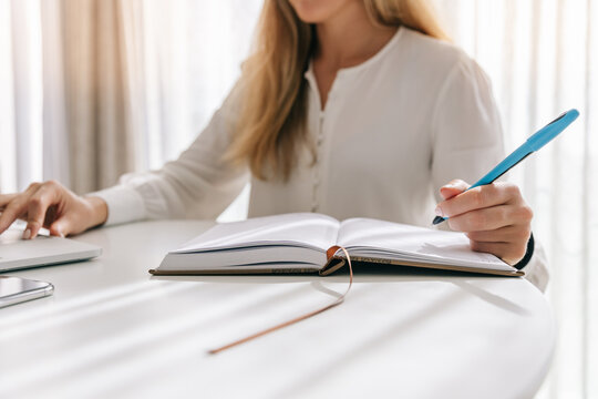 Woman writing in diary and using laptop on table