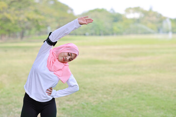 Public exercise lifestyle concept, fitness woman listening music from wireless earphones and mobile phone.  Athletic young asian girl in muslim sportswear standing, stretching after workout