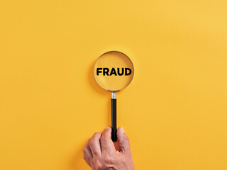 Male hand holds a magnifier focusing on the word fraud. To search, find, discover or reveal a fraud...