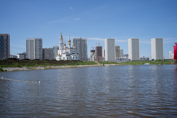 Naklejka premium The Russian Orthodox Church stands on the banks of the river against the backdrop of modern houses. High quality photo