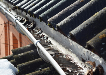 Roof gutter cleaning. A clogged rain gutter of an asbestos roof with non flowing water from melted...