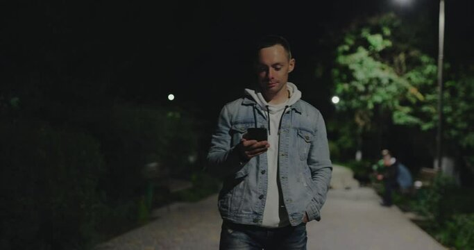 Man using smartphone walking along a night park