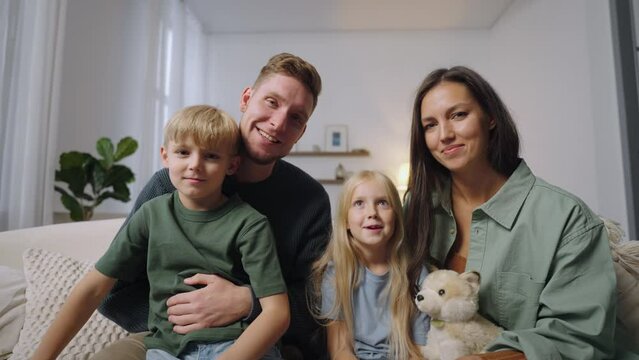 Parents with two children look into the camera and greet the interlocutor smiling waving their hands. A man and a woman calling friends on a webcam and talking smiling. talking on video communication