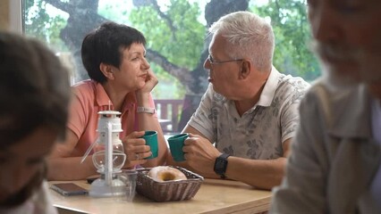 Lovely time. Cheerful smiling mature couple relaxing and hugging at indoor cafe table. Good looking sincere aged couple talking while drinking coffee and relaxing at the restaurant