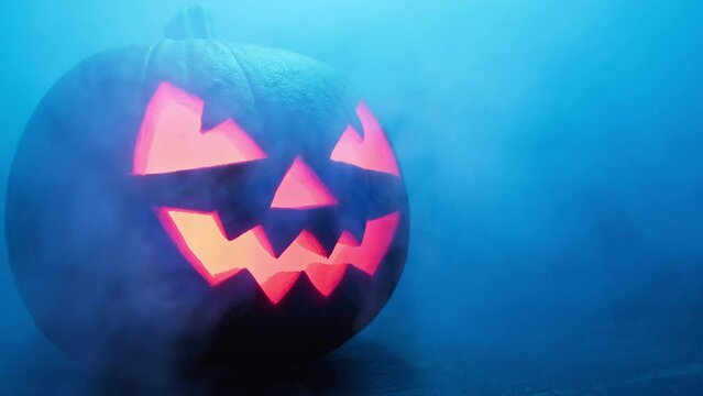Halloween scary pumpkin with smoke at dark background. Halloween pumpkin smile and scary glowing eyes. Jack O' Lantern symbol. Spooky face glowing in dark. Horror. Copy space. Close-up in 4K, UHD