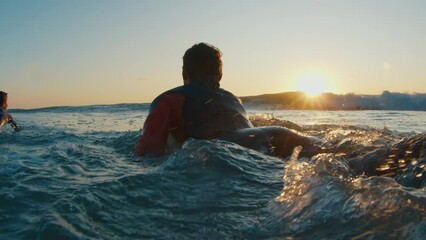 Male surfer paddles in the ocean at sunrise