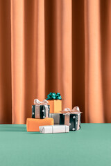 Minimal Christmas mood concept with orange gifts and green bow on orange curtain background. Fall and winter giveaway aesthetic. New year shopping and sale idea.