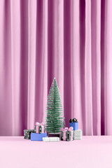 Minimal Christmas present concept with violet purple gifts with bows under the pine tree on a pastel pink curtain background. Giving season, New Year, festive, winter aesthetic.
