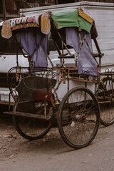 Fototapeta na wymiar photo of a rickshaw parked in front of white pick up car at traditional market during the day