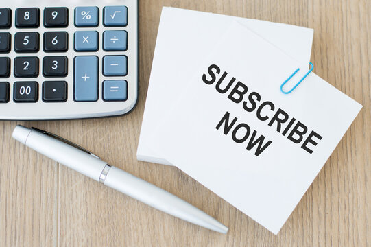 SUBSCRIBE NOW text on a card on a wooden background next to it lies a pen and a calculator