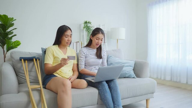 Asian woman amputee using laptop computer with friend in living room.