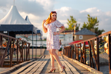 Fototapeta na wymiar A beautiful young woman in a dress poses standing on a sea pier. Summer vacation and carefree