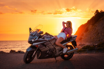 Fototapeta na wymiar Caucasian young woman lying posing on a motorcycle. Golden sunset and ocean on the background. Copy space. Freedom and motorcycle trips