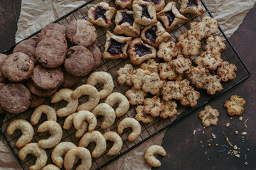 freshly baked Christmas cookies on a cake grid, different varieties like vanilla crescents and pastries with chocolate and marmalade