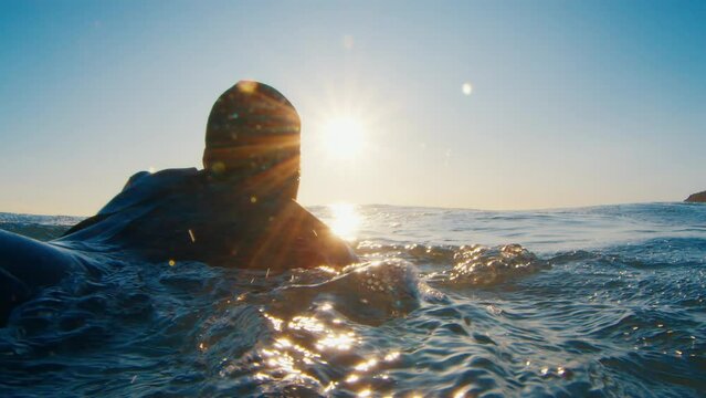 Male surfer paddles in the ocean at sunrise