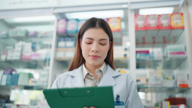A professional woman pharmacist rechecks products in a pharmacy and using a noteboard to write information.