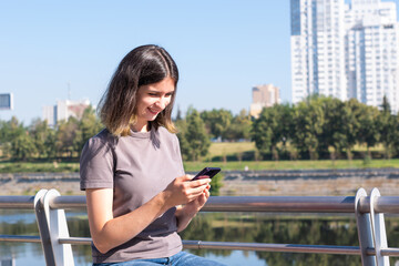 The concept of a freelancer. A beautiful brunette student with glasses uses a smartphone on the street. A beautiful student girl uses the phone, types SMS, communicates in an online chat