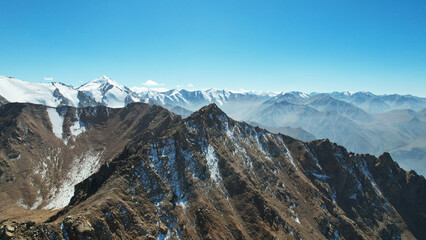Snowy rocky mountain peaks in a light haze. Aerial view from the drone of the blue sky, light haze...