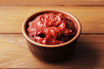 A bowl full of tomato sauce on a wooden background.