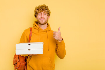 Young student man holding pizzas isolated on yellow background smiling and raising thumb up