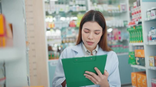 A professional woman pharmacist rechecks products in a pharmacy and using a noteboard to write information.