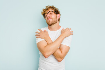 Young caucasian man isolated on blue background hugs, smiling carefree and happy.