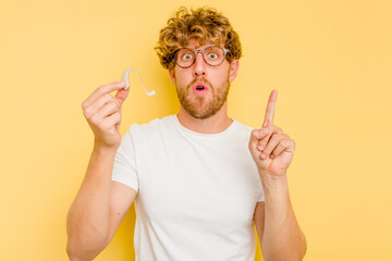 Young caucasian man wearing hearing aid isolated on yellow background having some great idea, concept of creativity.