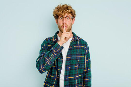 Young caucasian man isolated on blue background keeping a secret or asking for silence.