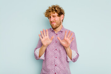 Young caucasian man isolated on blue background rejecting someone showing a gesture of disgust.