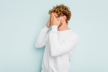 Young caucasian man isolated on blue background afraid covering eyes with hands.