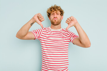 Young caucasian man isolated on blue background showing a dislike gesture, thumbs down. Disagreement concept.