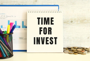 A notebook with the text TIME FOR INVEST is leaning against the wall with a folder with charts.
