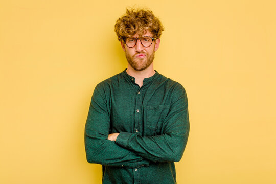 Young caucasian man isolated on yellow background frowning face in displeasure, keeps arms folded.