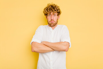 Young caucasian man isolated on yellow background shrugs shoulders and open eyes confused.