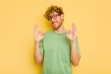 Young caucasian man isolated on yellow background cheerful and confident showing ok gesture.