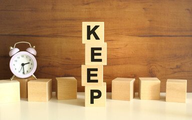 Four wooden cubes stacked vertically on a brown background form the word KEEP.