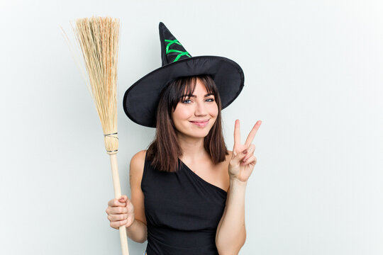 Young caucasian woman dressed as a witch holding a broom isolated on blue background showing number two with fingers.